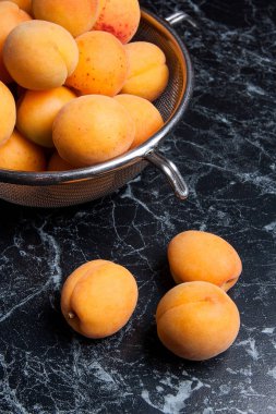 Olgun organik kayısı çelik kevgir içinde. Kompozisyon rustik tarzı - çelik kevgir içinde organik sarı sulu kayısı ve karanlık mermer zemin üzerine bütün ve yarıya kayısı. Sağlıklı gıda kavramı. Hasat zamanı