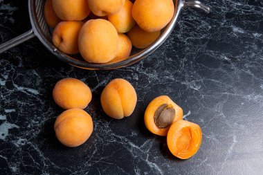 Olgun organik kayısı çelik kevgir içinde. Kompozisyon rustik tarzı - çelik kevgir içinde organik sarı sulu kayısı ve karanlık mermer zemin üzerine bütün ve yarıya kayısı. Sağlıklı gıda kavramı. Hasat zamanı