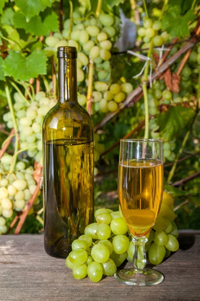 ブドウの束と白ワイン ブドウ畑の背景にヴィンテージの木製の背景の上にワインの瓶のガラス 背景としてブドウの葉を持つ枝にブドウの緑と黄色の果実の房 — ストック写真