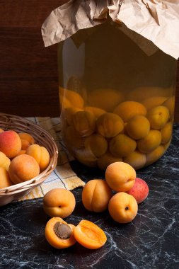 Tatlı Kayısı Kompostosu karanlık mermer üzerinde büyük cam kavanoz konserve ve yaz anda olgun organik kayısı hasat. Rustik tarzı - organik sarı sulu kayısı bütün ve yarıya sarı ahşap sepet ve ev yapımı Kayısı Kompostosu canne kompozisyon