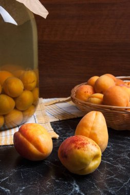 Tatlı Kayısı Kompostosu karanlık mermer üzerinde büyük cam kavanoz konserve ve yaz anda olgun organik kayısı hasat. Rustik tarzı - organik sarı sulu kayısı bütün ve yarıya sarı ahşap sepet ve ev yapımı Kayısı Kompostosu canne kompozisyon