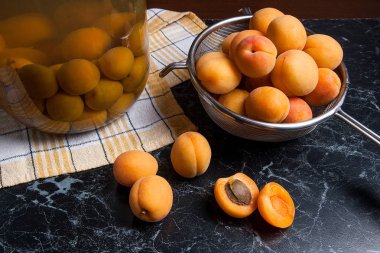 Tatlı Kayısı Kompostosu karanlık mermer üzerinde büyük cam kavanoz konserve ve yaz anda olgun organik kayısı hasat. Rustik tarzı - organik sarı sulu kayısı bütün ve çelik kevgir ve ev yapımı Kayısı Kompostosu b konserve yarıya kompozisyon