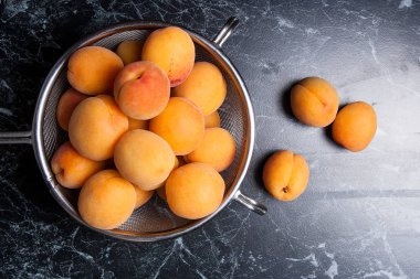 Olgun organik kayısı çelik kevgir içinde. Kompozisyon rustik tarzı - çelik kevgir içinde organik sarı sulu kayısı ve karanlık mermer zemin üzerine bütün ve yarıya kayısı. Sağlıklı gıda kavramı. Hasat zamanı