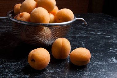 Olgun organik kayısı çelik kevgir içinde. Kompozisyon rustik tarzı - çelik kevgir içinde organik sarı sulu kayısı ve karanlık mermer zemin üzerine bütün ve yarıya kayısı. Sağlıklı gıda kavramı. Hasat zamanı