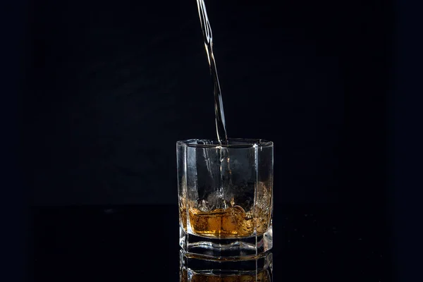 Uísque derramando em vidro com gelo isolado em fundo preto — Fotografia de Stock