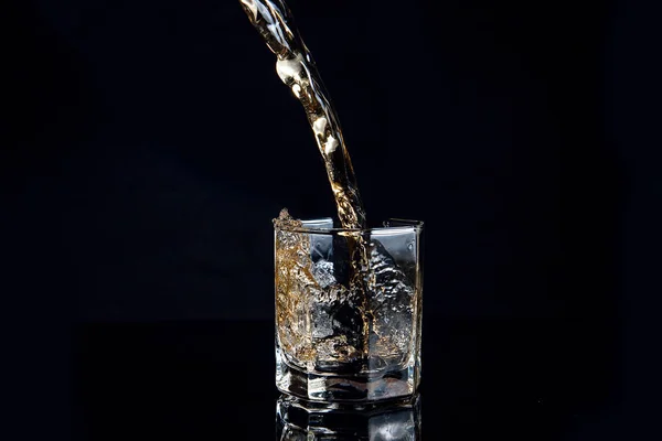 Whiskey pouring into glass with ice isolated on black background — Stock Photo, Image