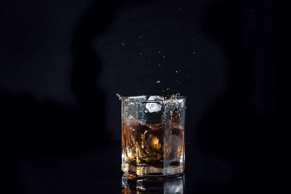 Whisky splash van de gevallen ijsblokje in glas met drank — Stockfoto