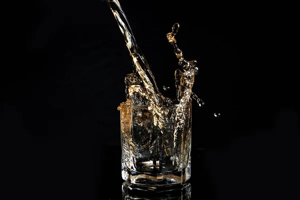 Whiskey pouring into glass with ice isolated on black background — Stock Photo, Image