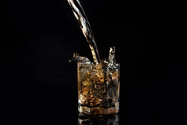 Whiskey pouring into glass with ice isolated on black background — Stock Photo, Image