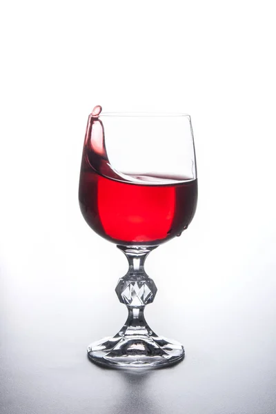 Rotwein spritzt im Weinglas auf hellem Hintergrund. — Stockfoto