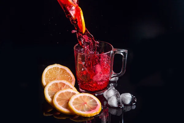 Hibiscus cold tea pouring into glass with ice, lemon and mint is