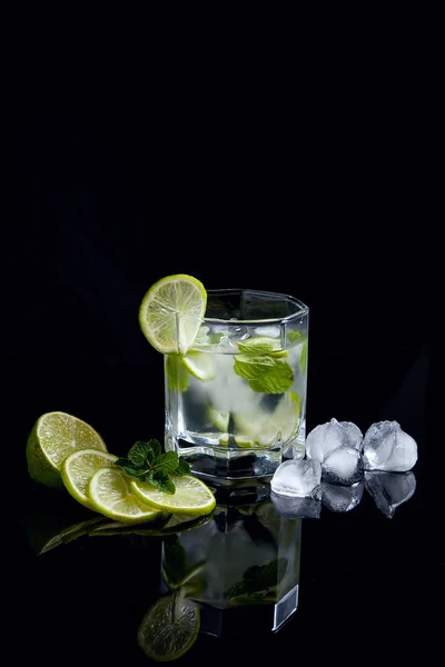 Summer cocktail mojito in glass, sliced lime and ice cubes on bl