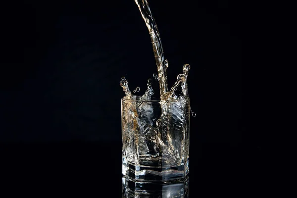 Whiskey pouring into glass with ice isolated on black background — Stock Photo, Image