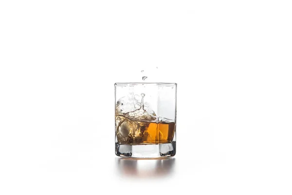 Брызги виски из падающего кубика льда в стекло с напитком — стоковое фото