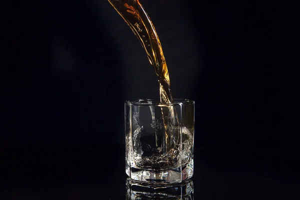 Uísque derramando em vidro com gelo isolado em fundo preto — Fotografia de Stock
