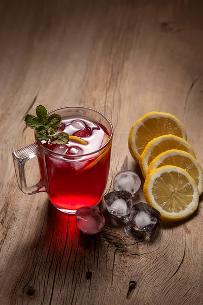 Hibiscus cold tea with ice, lemon and mint on vintage wooden bac