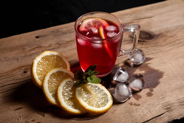 Hibiscus cold tea with ice, lemon and mint on vintage wooden bac