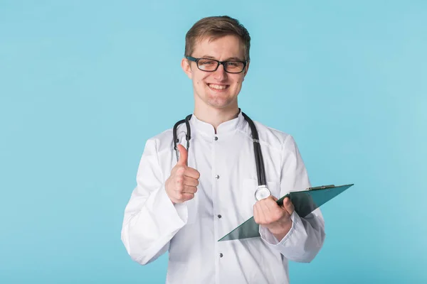 Lekarz medycyny, pisanie receptę na niebieskim tle pokazuje kciuk w — Zdjęcie stockowe