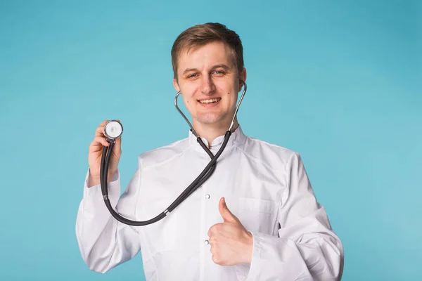 Lekarz z stetoskop Wyświetlono kciuk w na niebieskim tle — Zdjęcie stockowe