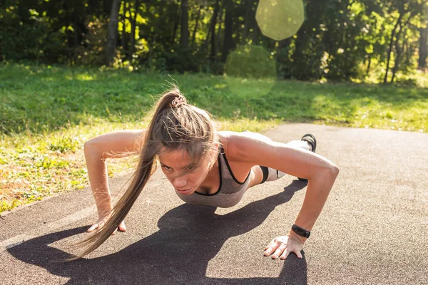 Fitness nő csinál fekvőtámaszokat szabadtéri kereszt-képzés edzés közben. Szép fiatal és fitt sport modell edzésprogram kívül a park — Stock Fotó