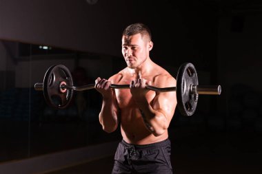 Güçlü vücut geliştirmeci barbell ile egzersizleri yapıyor. Koyu arka plan üzerinde çıplak gövde ile güçlü erkek. Güç ve motivasyon.