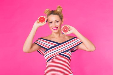 Greyfurt ile gülümseyen kız elinde pembe bir arka plan üzerinde yarım meyve kesme