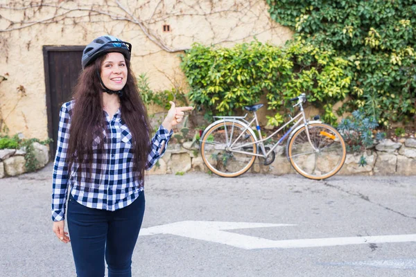 배경 골목에 자전거에 헬멧 행복 한 여자를 가리키는 — 스톡 사진