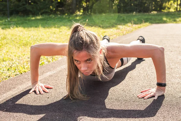 Fitness woman doing push-ups during outdoor cross training workout. Beautiful young and fit fitness sport model training outside in park