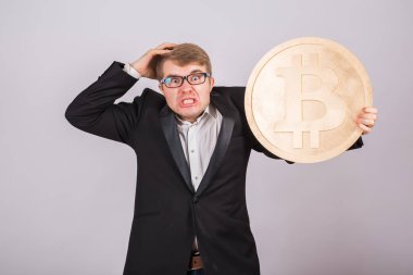 Kızgın bir işadamı portresi büyük altın bitcoin kollarında tutar. Adam cryptocurrency kazasında panik içinde