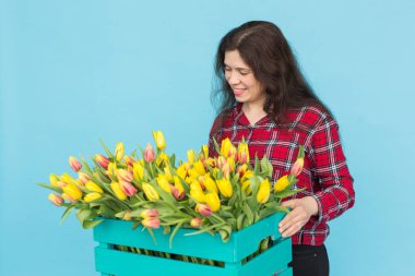 Lale mavi arka plan üzerinde kutu ile neşeli genç kadın çiçekçi