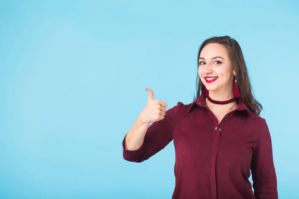 Alegre joven morena caucásica estudiante chica mostrando los pulgares hacia arriba sobre fondo azul con espacio de copia — Foto de Stock