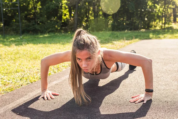 Femme de remise en forme faisant push-ups pendant l'entraînement cross extérieur. Belle jeune et forme physique sport modèle entraînement à l'extérieur dans le parc — Photo