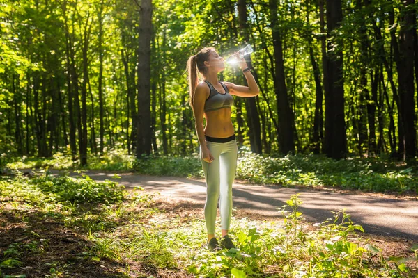 Fitness bela mulher bebendo água e sudorese depois de se exercitar no verão dia quente no parque. Atleta feminina após o exercício . — Fotografia de Stock