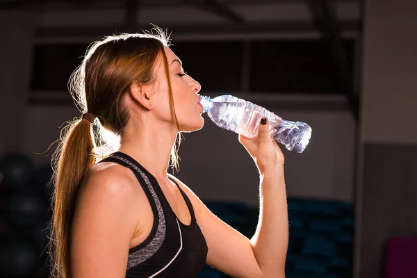 Фитнес молодая женщина пьет воду в тренажерном зале. Мышечная женщина делает перерыв после тренировки — стоковое фото