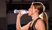 Fitness fiatal nő ivóvíz az edzőteremben. Izmos nő vesz break edzés után