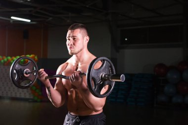 Güçlü vücut geliştirmeci barbell ile egzersizleri yapıyor. Koyu arka plan üzerinde çıplak gövde ile güçlü erkek. Güç ve motivasyon.