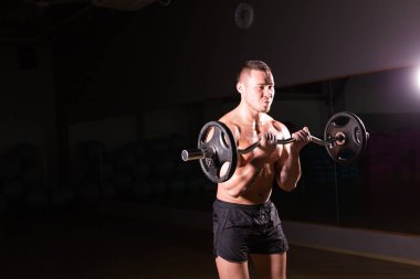 Güçlü vücut geliştirmeci barbell ile egzersizleri yapıyor. Koyu arka plan üzerinde çıplak gövde ile güçlü erkek. Güç ve motivasyon.