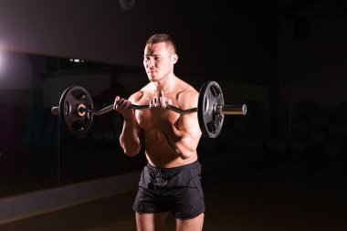 Güçlü vücut geliştirmeci barbell ile egzersizleri yapıyor. Koyu arka plan üzerinde çıplak gövde ile güçlü erkek. Güç ve motivasyon.