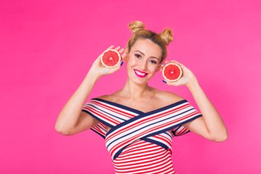 Greyfurt ile gülümseyen kız elinde pembe bir arka plan üzerinde yarım meyve kesme