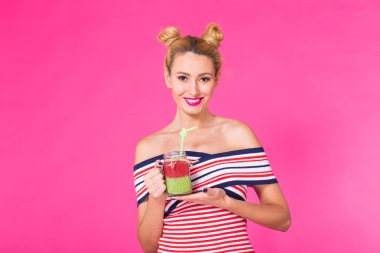 Holding ve lezzetli yeşil smoothie milkshake içme, pembe arka plan parlak kıyafeti giymiş komik genç kadın portresi studio kapatın