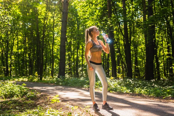 Fitness bela mulher bebendo água e sudorese depois de se exercitar no verão dia quente no parque. Atleta feminina após o exercício . — Fotografia de Stock