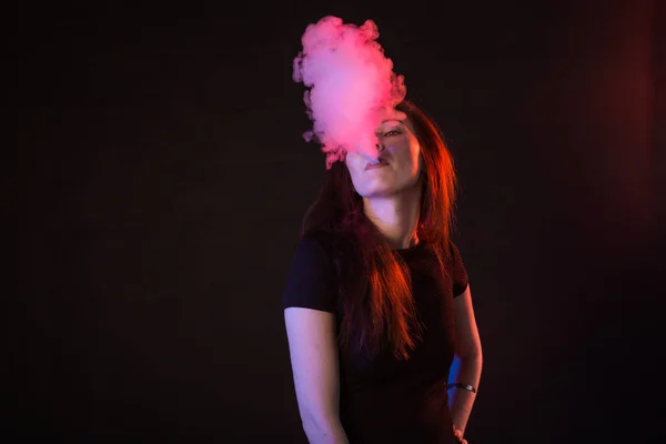 Молодая женщина курит электронные сигареты на темном фоне — стоковое фото