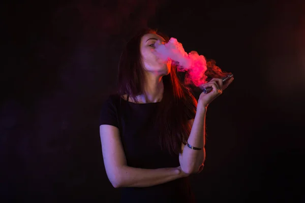 Jeune femme fumant cigarette électronique sur fond sombre — Photo