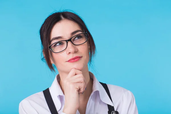 Portret atrakcyjne zadumany zamyślony młoda kobieta w okularach z jej palec do jej podbródek, patrząc w górę w kontemplacji na niebieskim tle — Zdjęcie stockowe