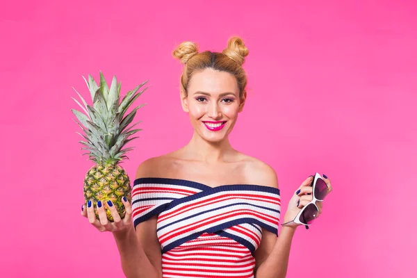 Bir ananas boşaltmak ile pembe bir arka plan üzerinde tutan mutlu genç kadın. Yaz, diyet ve tatil kavramı