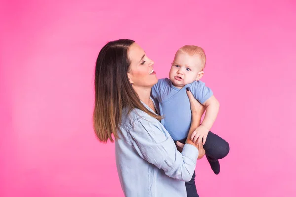 Feliz jovem mãe com um bebê criança no fundo rosa — Fotografia de Stock