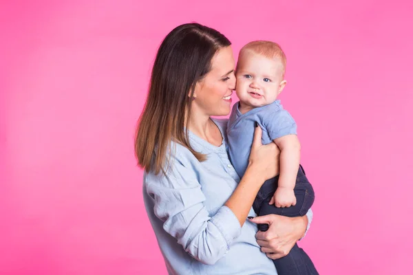 Madre cariñosa jugando con su bebé sobre fondo rosa — Foto de Stock