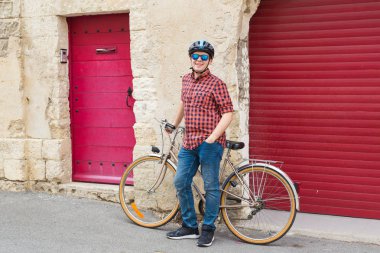 Genç adam, kask, güneş gözlüğü ve kırmızı gömlek tutun Bisiklet artalan kırmızı açık