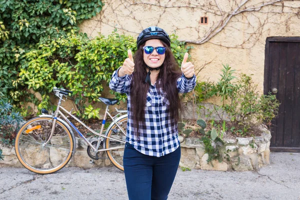 헬멧과 선글라스 배경 자전거 및 거리에 엄지손가락을 나타나고에 여자 — 스톡 사진