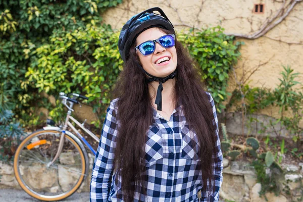 Mulher feliz sorriso com capacete e óculos de sol posição no fundo bicicleta e beco — Fotografia de Stock